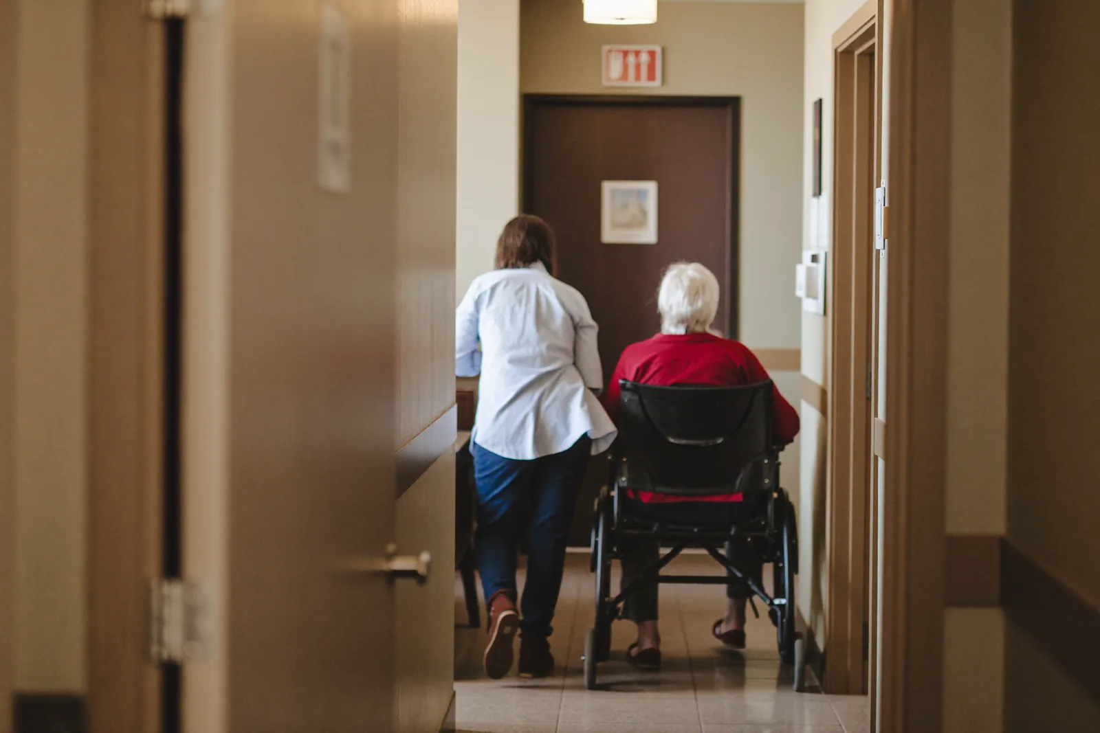 Caregiver walking beside a resident in a secured memory care hallway