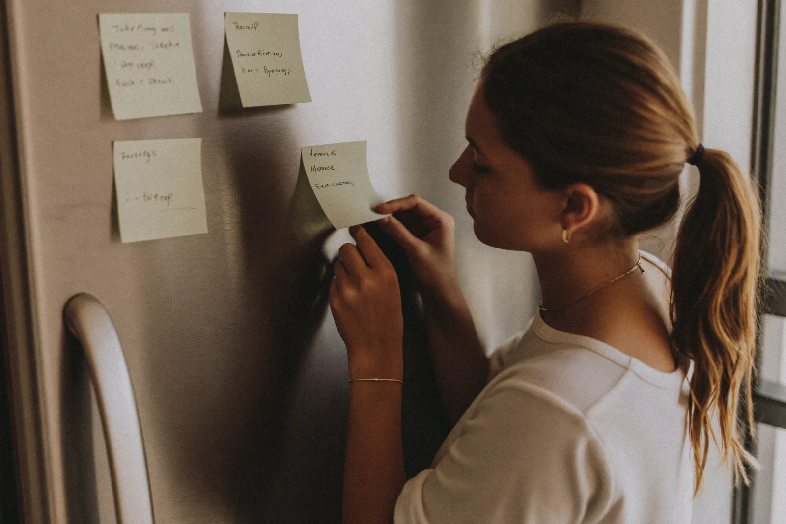 Adult daughter noticing many sticky note reminders on a refrigerator