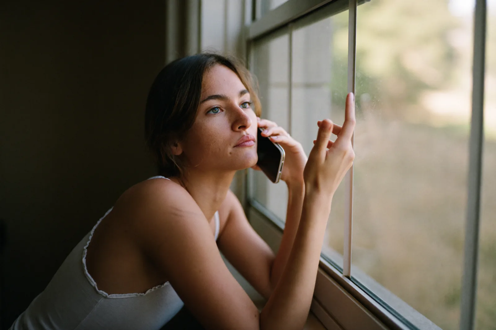 Adult daughter holding a phone thoughtfully at her kitchen window