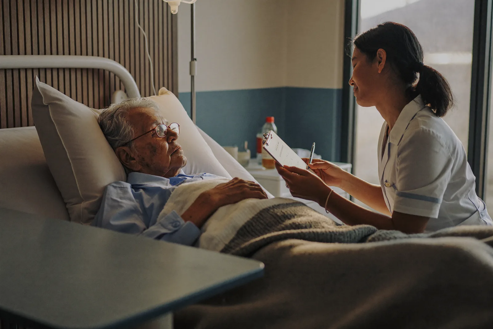 Nurse checking a chart while a resident rests in a skilled nursing room