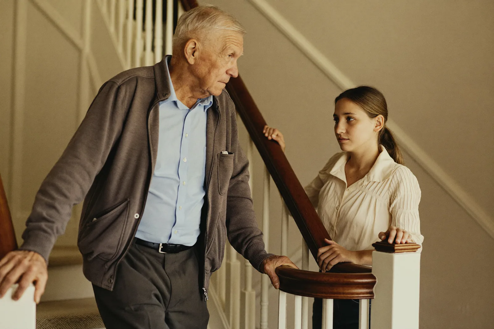 Elderly man steadying himself on a stair rail while his daughter watches