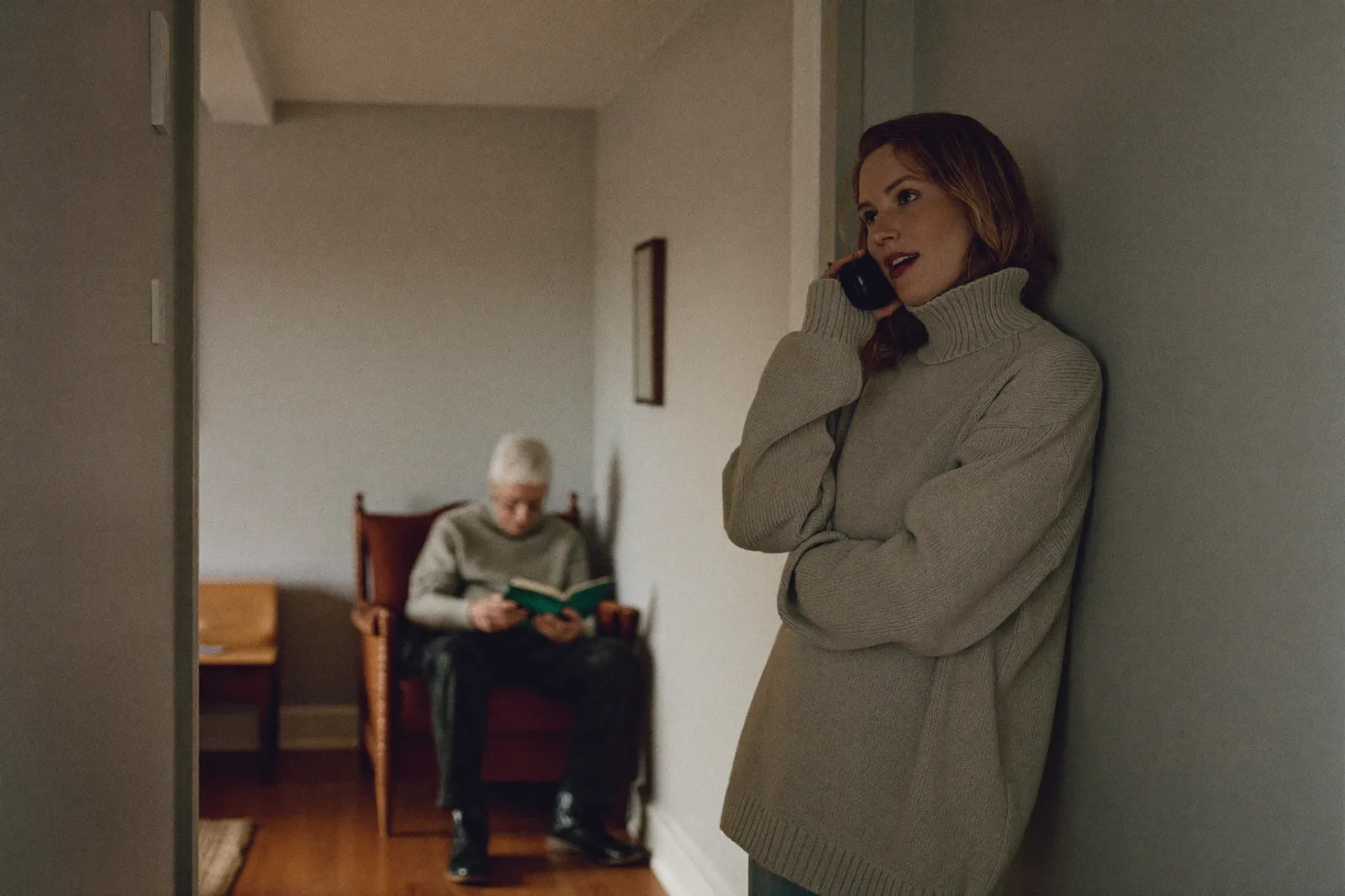 Adult daughter on the phone in a hallway while her father reads